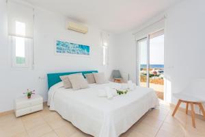 a white bedroom with a bed and a view of the ocean at Binicasal in Sant Lluis