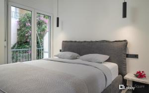 a white bedroom with a bed and a window at La Mer Apartment by LobbySquare in Piraeus
