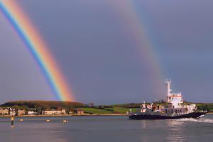 a boat in the water with a rainbow in the background at Cottage at the Alms - Dog Friendly! in Strangford