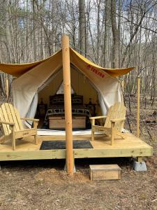 a tent with two chairs and a bed in the woods at Tentrr Signature Site - 6 Ponds Farm Glamping in Morganton