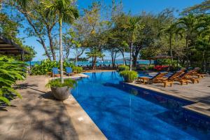 a swimming pool with chairs and the ocean in the background at Jet Luxury at Langosta Beach Resort & Villas in Tamarindo
