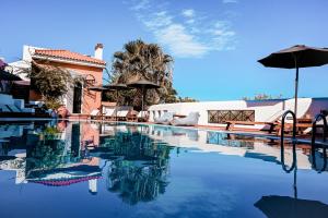 a swimming pool with an umbrella and chairs and a house at Nisea Hotel Samos in Pythagoreio