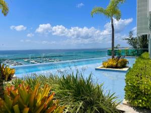 een zwembad met een palmboom en de oceaan bij Cloc Marina Vista Mar p/ a Baía de Todos os Santos in Salvador