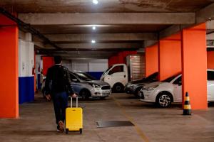Um homem a atravessar uma garagem com uma mala amarela. em Luds Comfort Hotel em Ponta Grossa