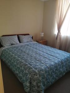 1 dormitorio con 1 cama con edredón azul y ventana en Departamento de 3 habitaciones frente a la universidad de Talca, en Talca