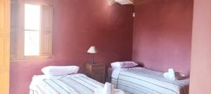 2 Betten in einem Zimmer mit roten Wänden und einem Fenster in der Unterkunft La Elegida in Tilcara