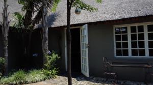 a cottage with a thatch roof and a door at Little Eden Guest Lodge in Vanderbijlpark