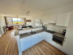 a kitchen with white cabinets and a living room at Appartementen Zeezicht in Katwijk aan Zee