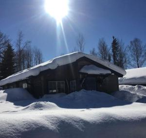 a house covered in snow with the sun behind it at StugaNäraKungsberget - mysig stuga med kamin, grillkåta och vedbastu in Ockelbo
