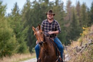 Um homem de chapéu de cowboy a andar a cavalo por uma estrada. em Gruberhof Coll em Funes