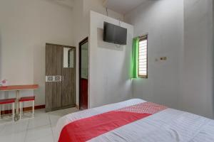 um quarto com uma cama e uma televisão na parede em Capital O 91690 Moza Guest House em Klaten