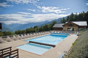 a swimming pool with chairs and mountains in the background at Résidence La Marmottane in Aime