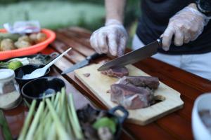 a person cutting meat on a cutting board with a knife at Mama Tia Family Homestay in Rantepao