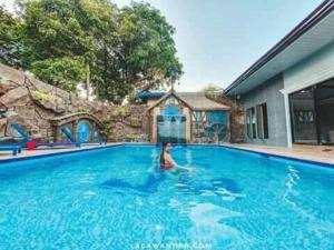 une femme nageant dans une grande piscine bleue dans l'établissement The Shire Private Resort, à Bago