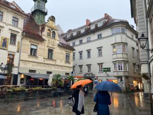 dos personas caminando por una calle bajo la lluvia con sombrillas en Carillon by BestChoice - Old City - Self Check-in with PARKING option en Graz