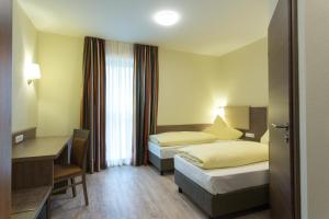 a hotel room with two beds and a desk at CityApart Hotel in Dingolfing