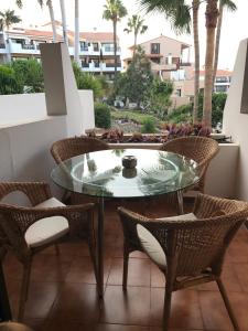 een glazen tafel en stoelen op een balkon met palmbomen bij Royal park albatros bonito apartamento Golf del Sur in San Miguel de Abona