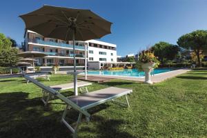 a bench with an umbrella next to a pool at Hotel Falcone in Lignano Sabbiadoro