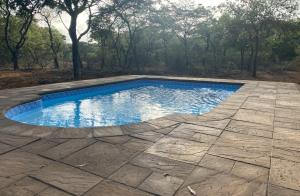 a swimming pool with a stone patio and trees at Vlakkieskraal Farmstay - Nyala Tented Camp in Bela-Bela