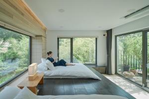 a woman sitting on a bed in a room with large windows at Scenery after Rain in Yangyang