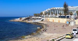 una spiaggia con persone sulla sabbia e un edificio di In the Heart of Bugibba a San Pawl il-Baħar