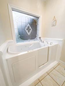 La salle de bains est pourvue d'une baignoire blanche et d'une fenêtre. dans l'établissement Spacious King Suite Mid Town Home With Serene Patio, à Hattiesburg