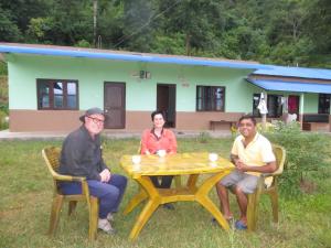 três pessoas sentadas numa mesa em frente a uma casa em Gorkha Organic Agro Farm em Gorkhā
