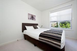 a white bedroom with a bed and a window at Trieste Apartments Kingston ACT in Canberra