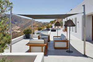 balcón con muebles blancos y vistas a las montañas en Kamini Santorini Villas, en Pirgos