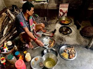 um homem a cozinhar comida numa mesa com tigelas de comida em Satrangi Homestay Sundarban em Kākdwīp