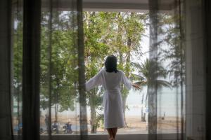 Anona Beachfront Phuket Resort-SHA EXTRA PLUS في شاطيء باتونغ: امرأة ترتدي ثوب أبيض تتطلع من النافذة