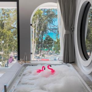 Anona Beachfront Phuket Resort-SHA EXTRA PLUS في شاطيء باتونغ: حوض استحمام مع فلامنغو وردي في غرفة مع نافذة