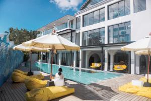 a building with a pool with yellow chairs and umbrellas at Anona Beachfront Phuket Resort-SHA EXTRA PLUS in Patong Beach