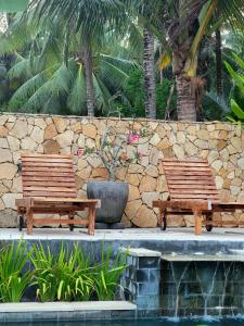 2 bancos de madera sentados junto a una pared de piedra en Drift Hideaway, en Kuta Lombok