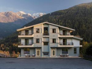 a large white building with mountains in the background at Hotel Garnì Alta Valle in Ponte di Legno