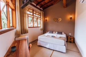 a bedroom with a bed and a table and windows at VELINN Pousada Villa Caiçara in Ilhabela