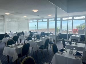 un restaurante con mesas y sillas blancas y ventanas en Channel View Hotel en Shanklin