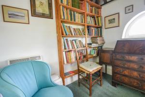 a room with a chair and a book shelf with books at Greystones Cottage in Chideock