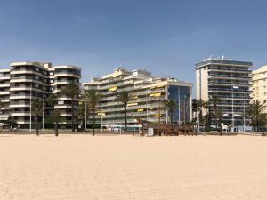 einen Strand mit Gebäuden und Palmen vor einem Gebäude in der Unterkunft Aguamarina Gandia in Playa de Gandia