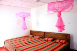 アヌラーダプラにあるDula Lake Resortのベッドルーム1室(カラフルなシーツとピンクのカーテンが備わるベッド1台付)