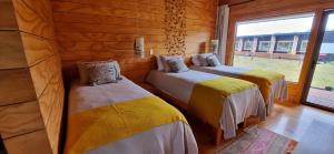 three beds in a wooden room with a window at Rumbo Sur Hotel in Villa O'Higgins
