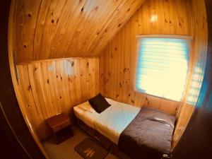 uma pequena cama num quarto de madeira com uma janela em Cabañas Queltehue Ltda em Ancud