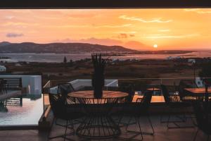 Kouros Blanc Resort & Suites في Pounda: طاولة وكراسي على شرفة مع غروب الشمس