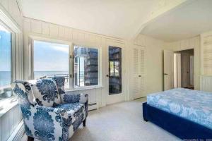a bedroom with a bed and a chair and windows at Direct Waterfront 4 Bedroom Beach House With Stunning LI Sound Views & Private Beach in Guilford