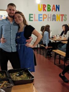 Un uomo e una donna in piedi accanto a un vassoio di cibo di Urban Elephants Hostel a Bratislava