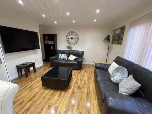 a living room with black leather furniture and a flat screen tv at 5 Bedroom House by monishortlets in Dagenham