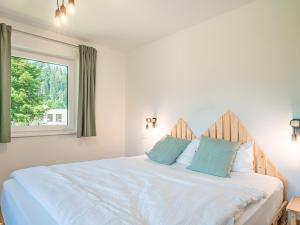Cama blanca con almohadas azules y ventana en Tirola Bude Sepp Top 4, en Hopfgarten im Brixental