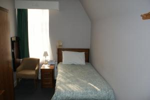 a bedroom with a bed and a chair and a window at Kirkdale Hotel in Croydon