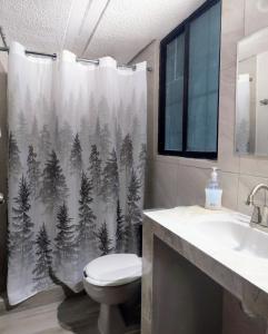 a bathroom with a toilet and a shower curtain with trees at El Depa del Puerto in Cancún