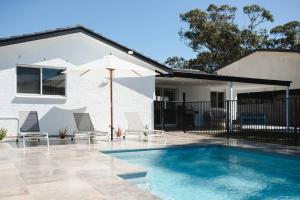 a pool with chairs and an umbrella next to a house at Seagrass in Culburra Beach